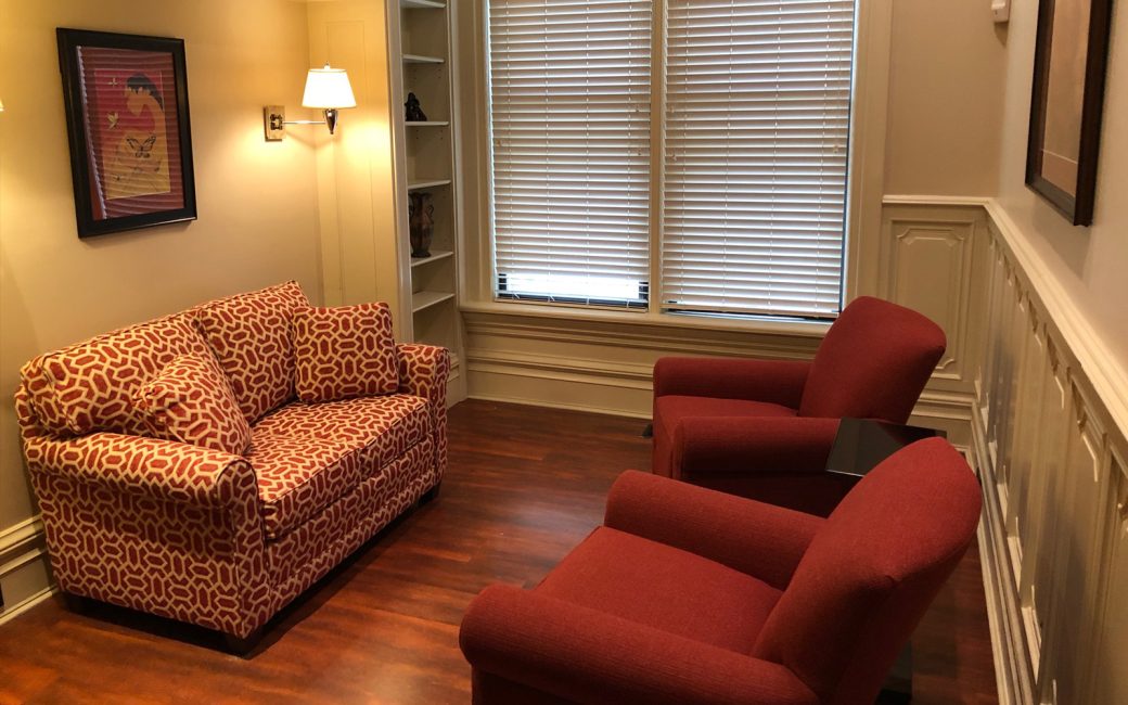 counseling room with cozy lighting and burgundy chairs and pink patterned couch